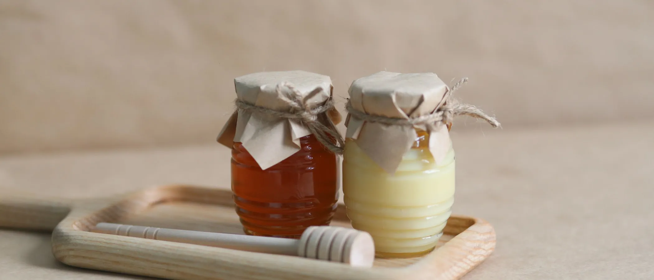 Two jars of honey on a wooden tray with a honey dipper, perfect for gourmet food styling.