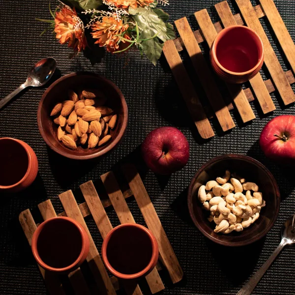 Warm rustic flatlay featuring apples, almonds, cashews, and wooden coasters.
