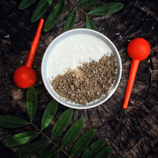 Top view of Nigerian kindirmo with granules on a wooden surface, styled with green leaves and red utensils.